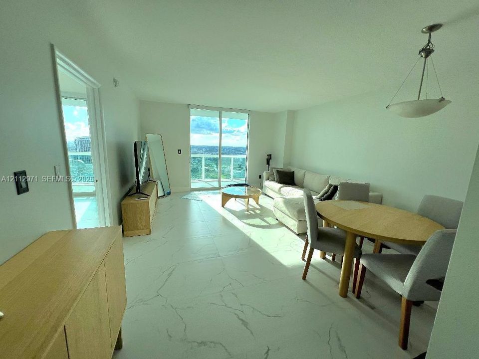Open-concept interior featuring large-format tile flooring with veining detail, floor-to-ceiling glass sliding doors, and a suspended pendant light fixture