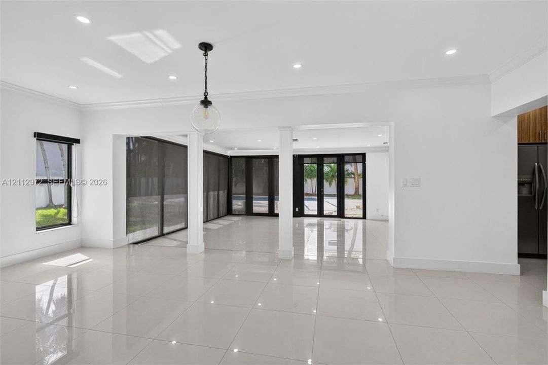 Large-format polished tile flooring, recessed ceiling lighting, structural support columns, black-framed sliding glass doors, and a decorative globe pendant fixture
