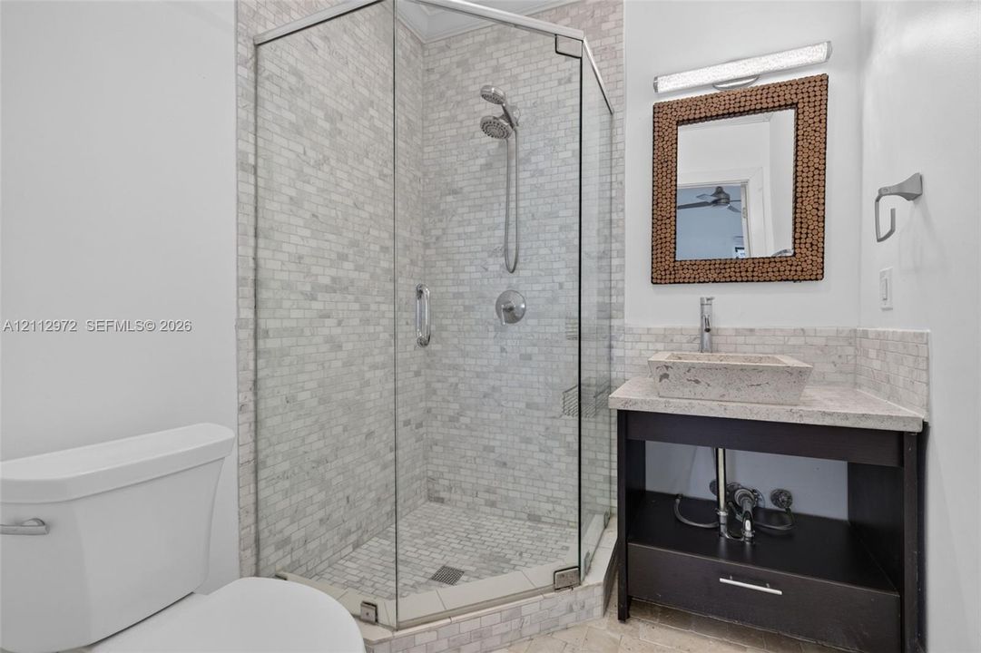 Corner shower enclosure with glass panels, stone-tiled walls, and a handheld showerhead