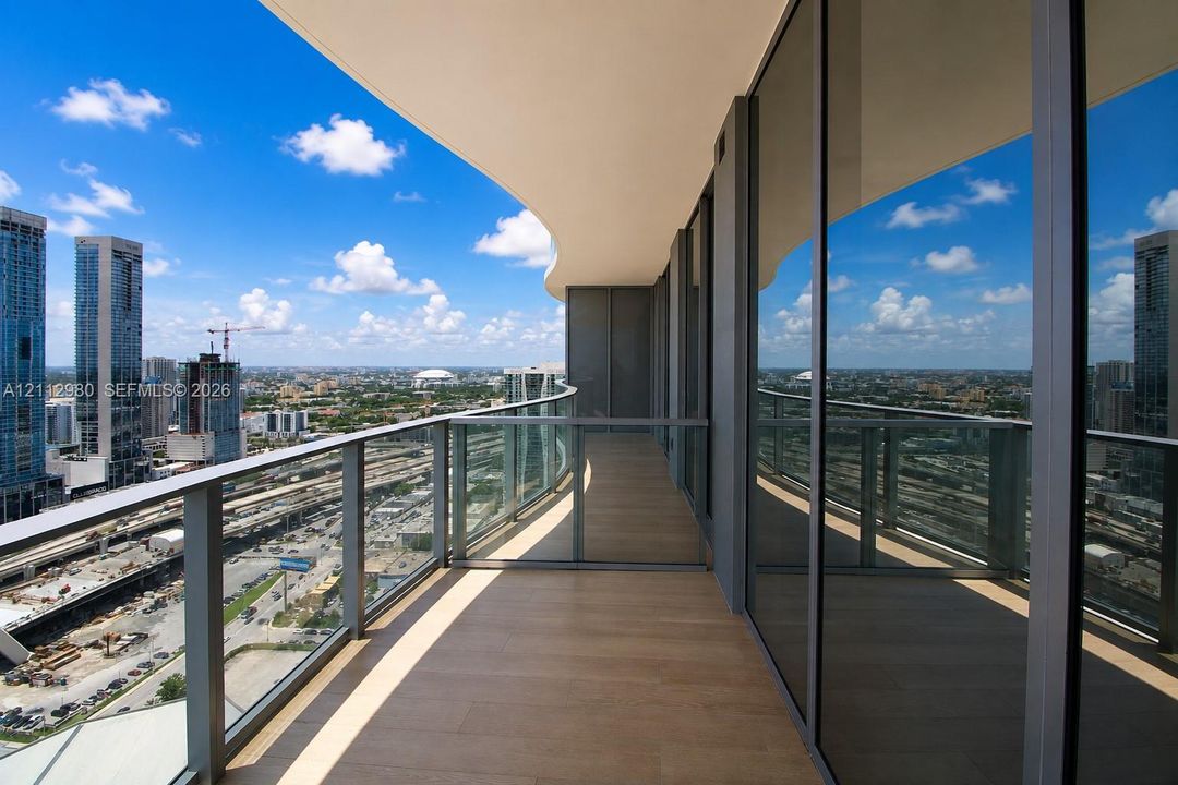 Curved balcony featuring wood-finish flooring, floor-to-ceiling glass paneling, metal railings, and wide-reaching urban skyline panoramas