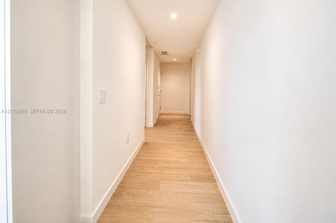 Hallway featuring neutral-toned walls, recessed lighting, and wood-finish flooring