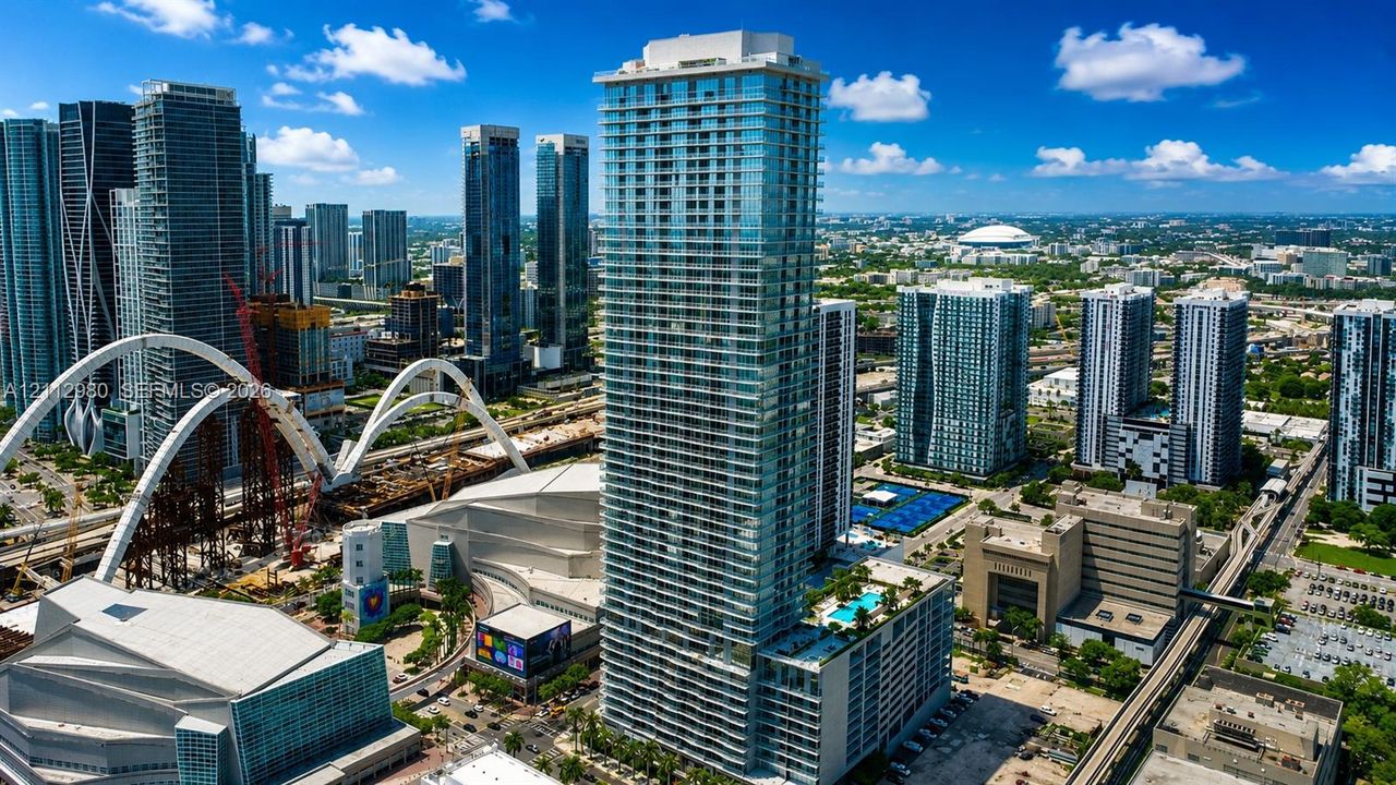 High-rise residential tower featuring a blue glass curtain wall, integrated multi-level parking structure, and a rooftop swimming pool with a surrounding deck