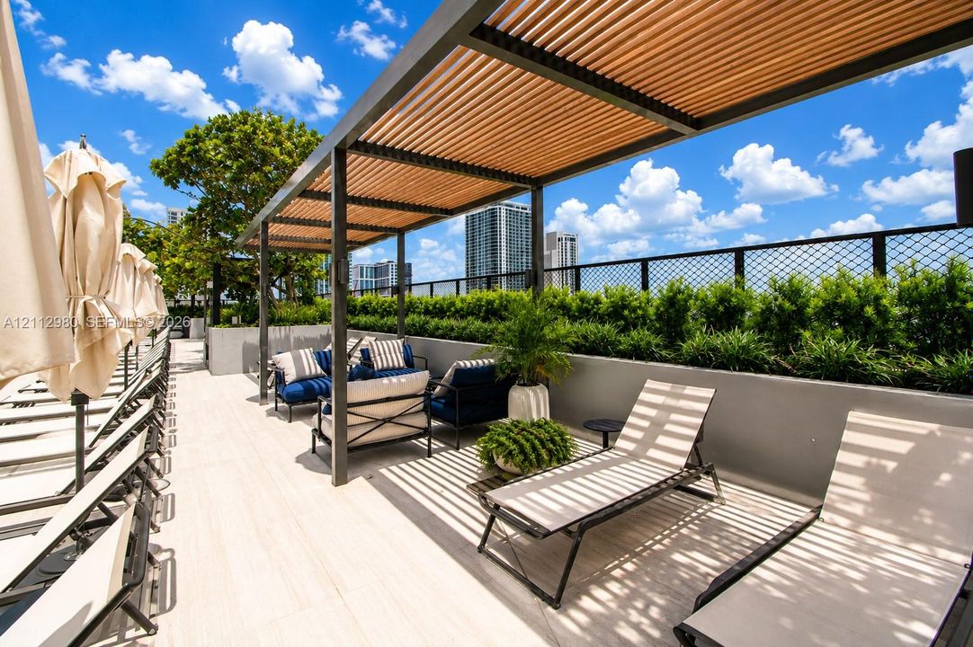 Rooftop terrace featuring light-toned tile flooring, a metal-framed pergola with wooden slat shading, and a perimeter planter wall with integrated greenery