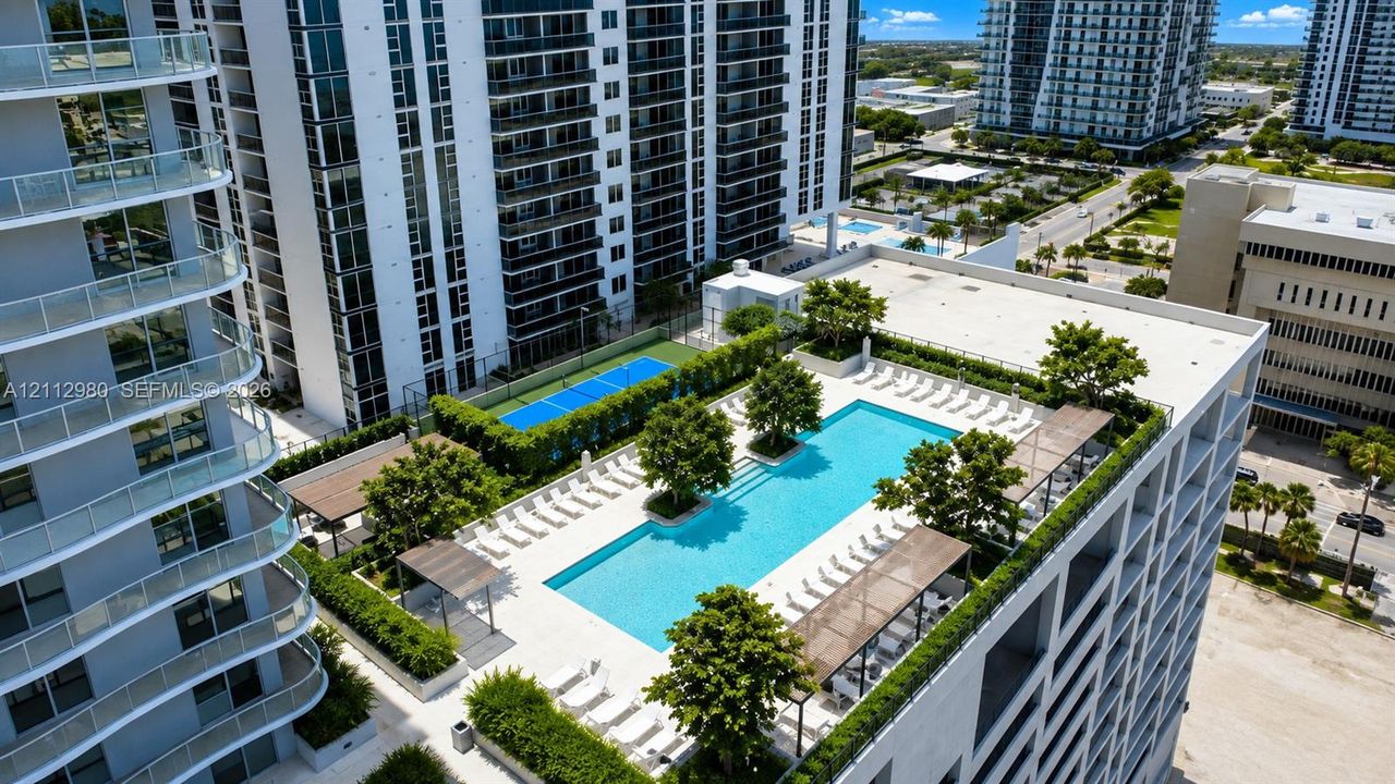 Rooftop recreation area featuring a swimming pool, sport court, shaded seating structures, and mature perimeter landscaping