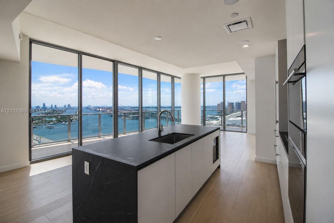 Kitchen featuring a dark stone island with an undermount sink, floor-to-ceiling glass windows, wood-finish flooring, white cabinetry, and built-in stainless steel appliances