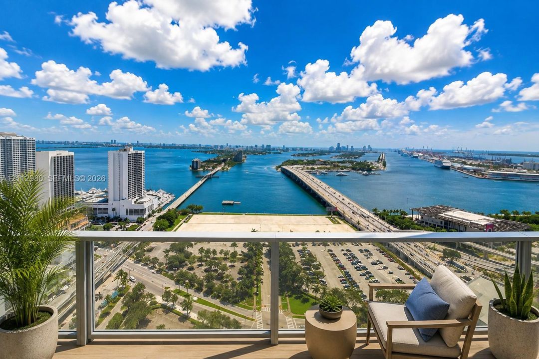 Private balcony featuring a glass-panel railing and wood-finish flooring with expansive coastal, waterway, and city infrastructure scenery