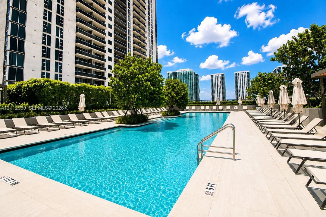 Swimming pool featuring a tiled deck, built-in metal handrails, integrated landscaping, and a rectangular basin