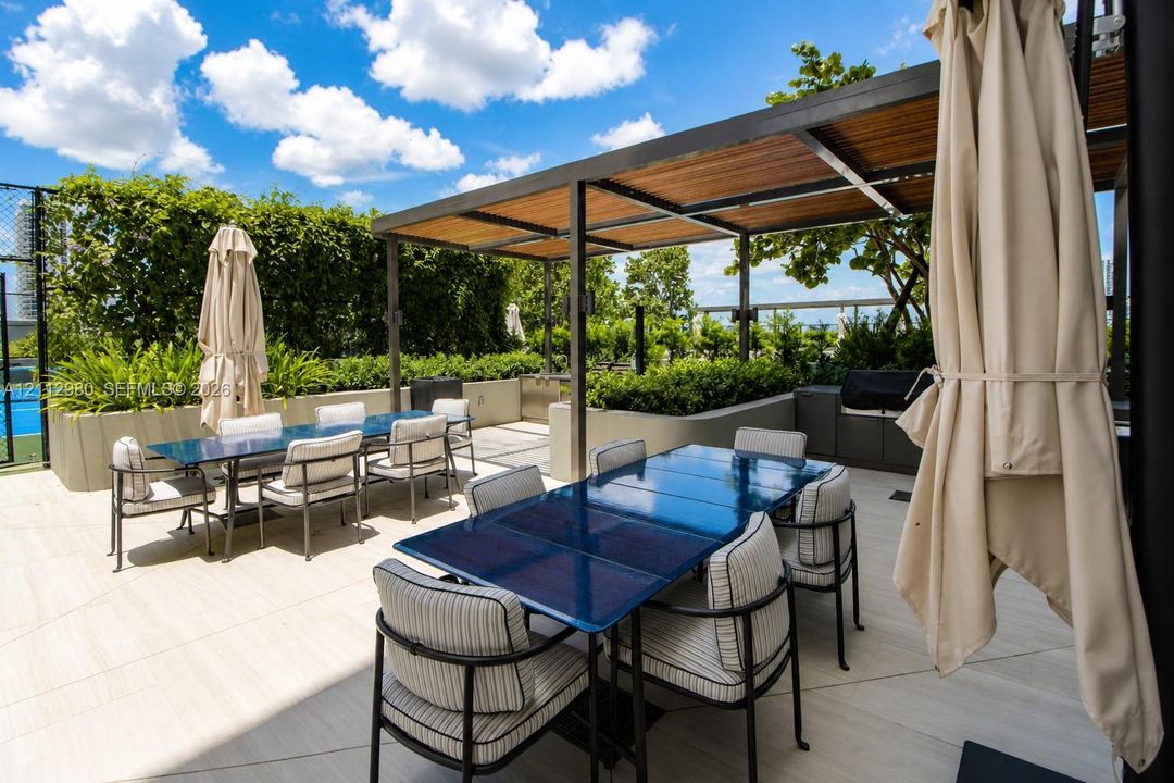 Outdoor terrace featuring porcelain tile flooring, a metal-framed pergola with wood-slat detailing, built-in cabinetry, and perimeter landscaping