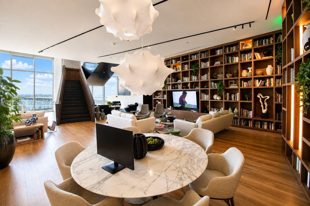 Floor-to-ceiling windows, wood-finish flooring, full-wall built-in shelving, sculptural pendant lighting, and a circular stone-top table