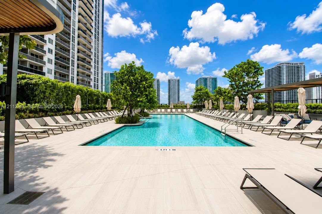 Rectangular swimming pool featuring neutral-toned tile decking, integrated landscaping, and metal pergola structures