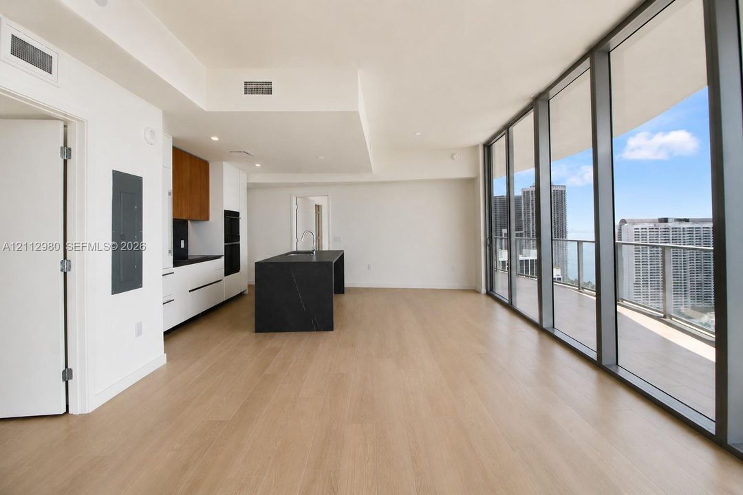 Modern kitchen featuring a dark stone-finish center island, floor-to-ceiling glass paneling, wood-finish flooring, built-in cabinetry, and integrated appliances