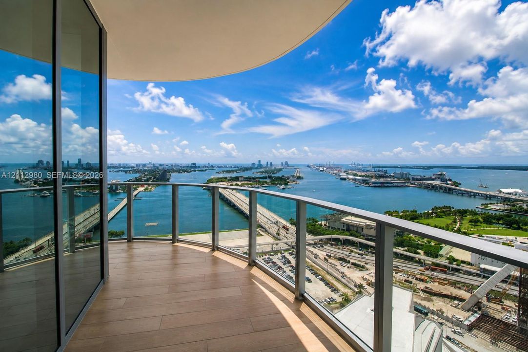 Curved balcony featuring wood-finish flooring, glass panel railings, and floor-to-ceiling glass wall panels