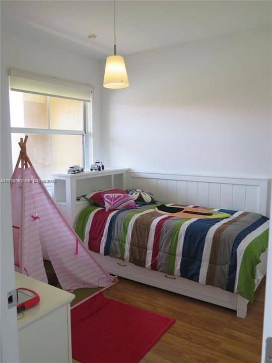 Bedroom featuring wood-finish flooring, a white beadboard-panel wall accent, a built-in headboard unit with shelving, and a pendant light fixture