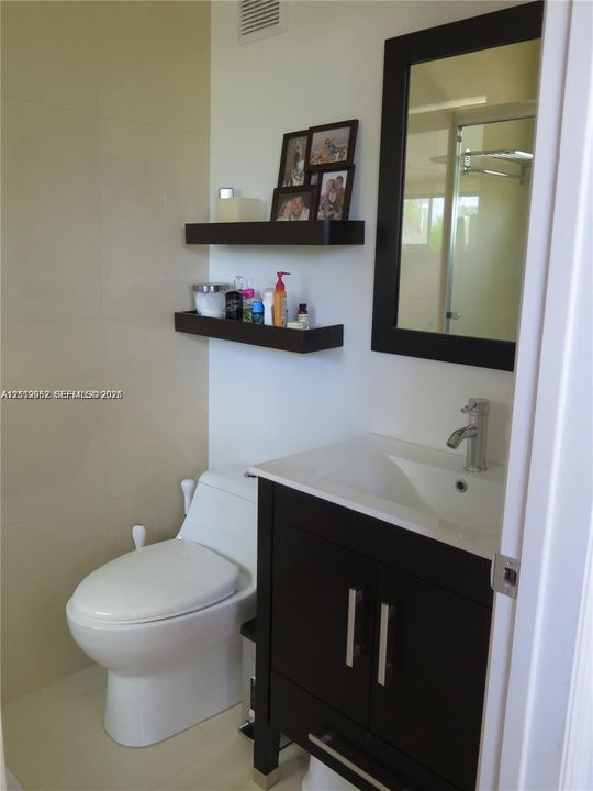 Dark wood-finish vanity with a white integrated countertop and basin, chrome faucet, matching wall-mounted mirror, and two floating shelves