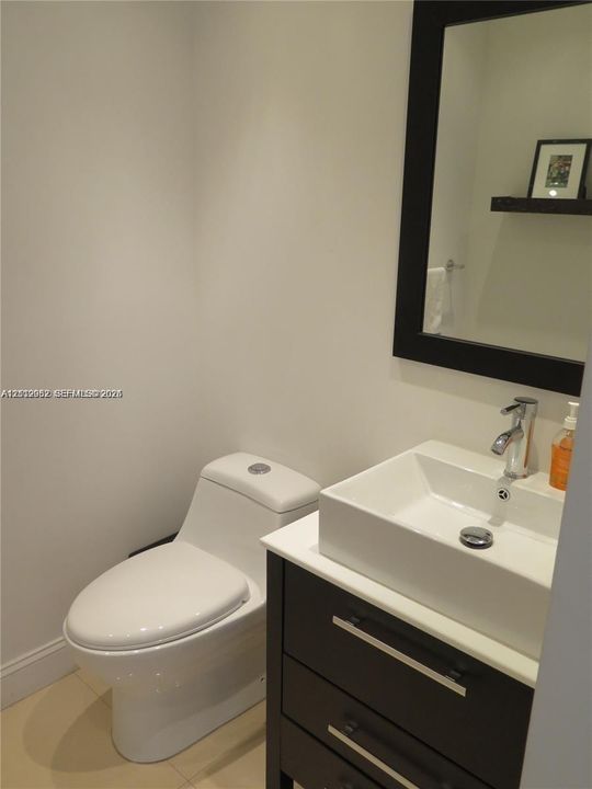 Dark-finish vanity with a white rectangular vessel sink, polished chrome faucet, stone-surfaced countertop, and framed mirror