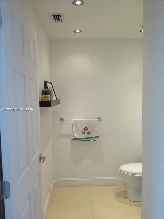 Recessed ceiling lighting, white ceramic commode, and light-toned tile flooring