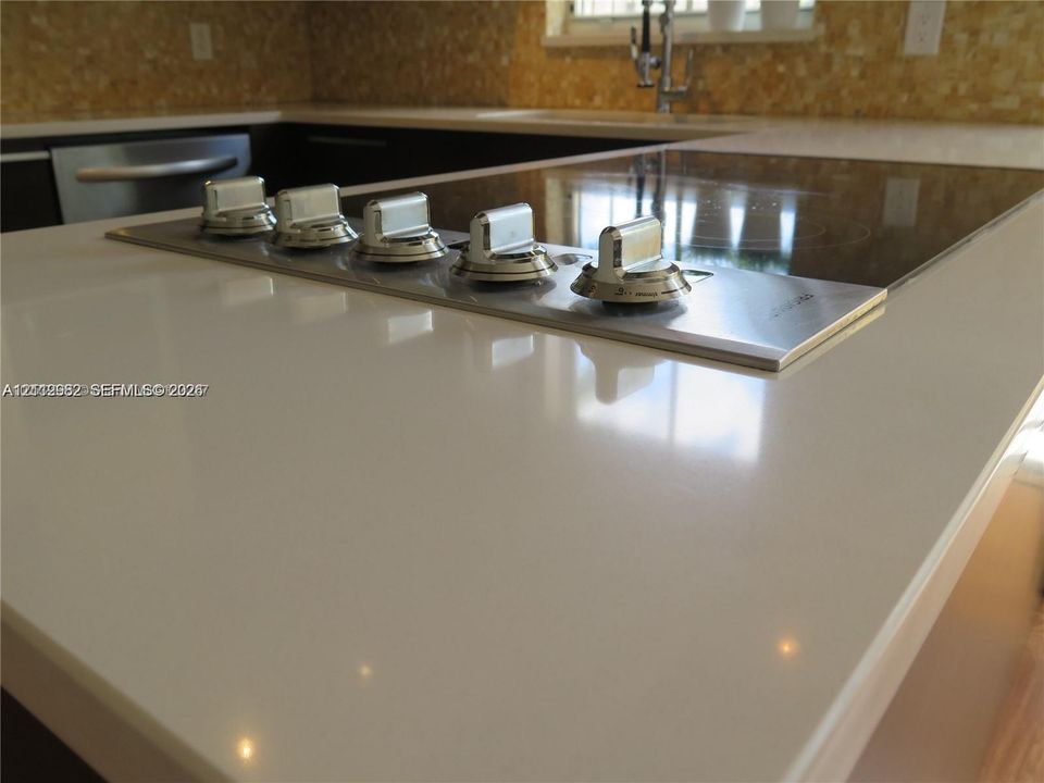 Solid-surface countertop with an integrated electric cooktop, stainless steel control knobs, and mosaic tile backsplash