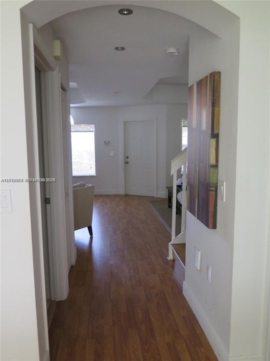 Arched entryway featuring wood-finish flooring, recessed ceiling lighting, and a partial staircase with a white balustrade