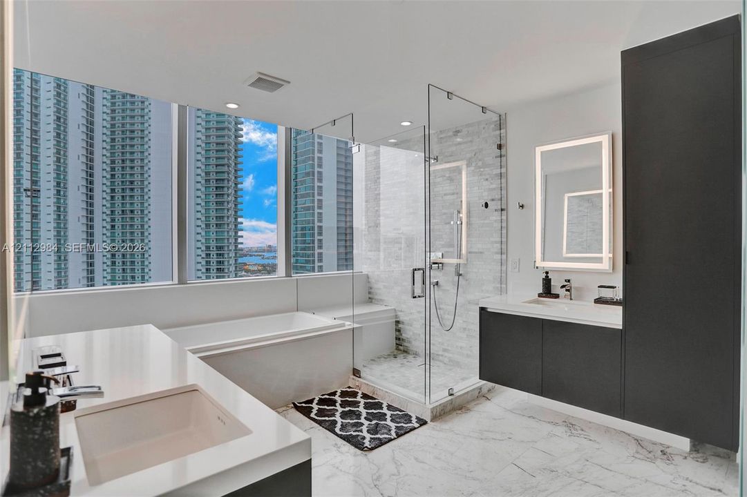 Bathroom featuring floor-to-ceiling windows, a deep soaking tub, a glass-enclosed walk-in shower with tile surround, a dual vanity with stone countertops, and full-height dark cabinetry