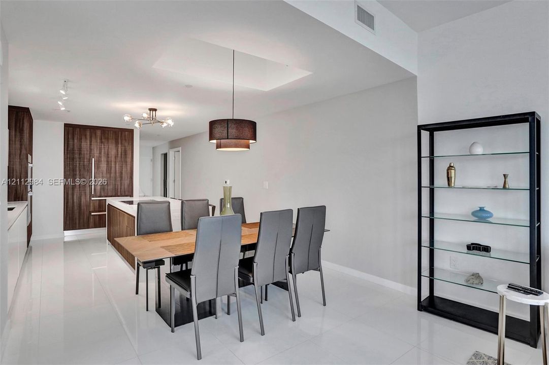 Kitchen and dining area featuring wood-finish cabinetry, a white countertop island, pendant lighting, and polished flooring