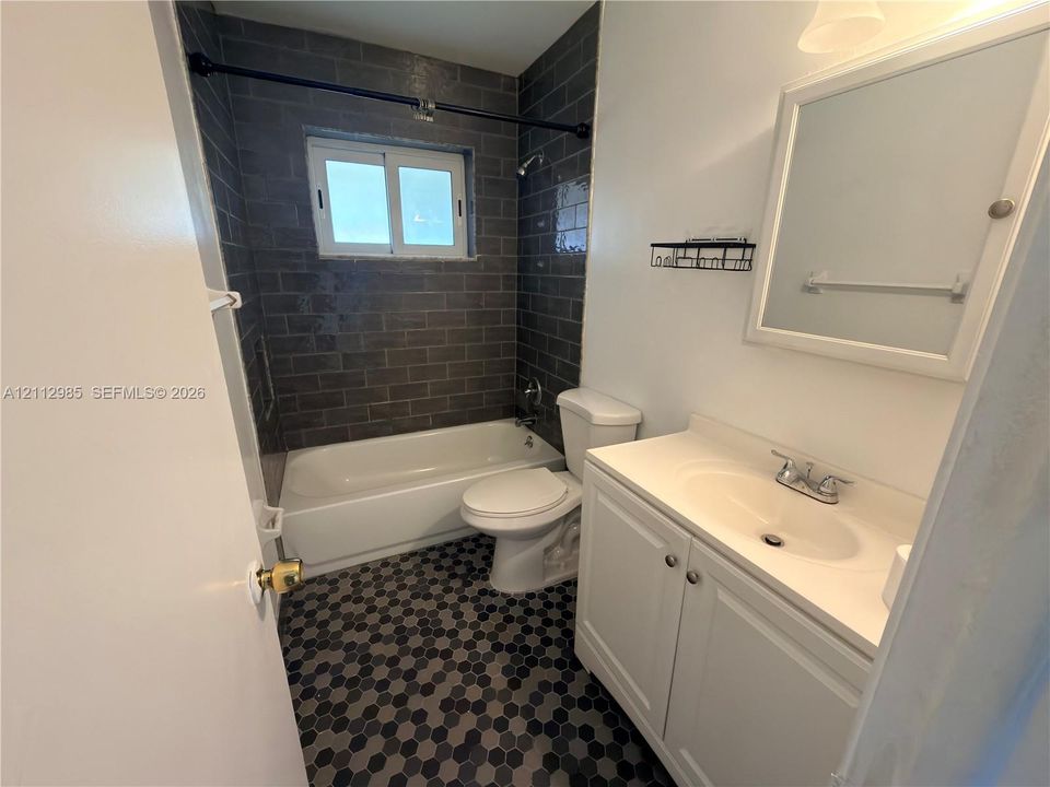 Bathroom featuring a white vanity cabinet with a integrated sink, dark charcoal subway-style tile shower surround, hexagonal floor tile, and a wall-mounted medicine cabinet