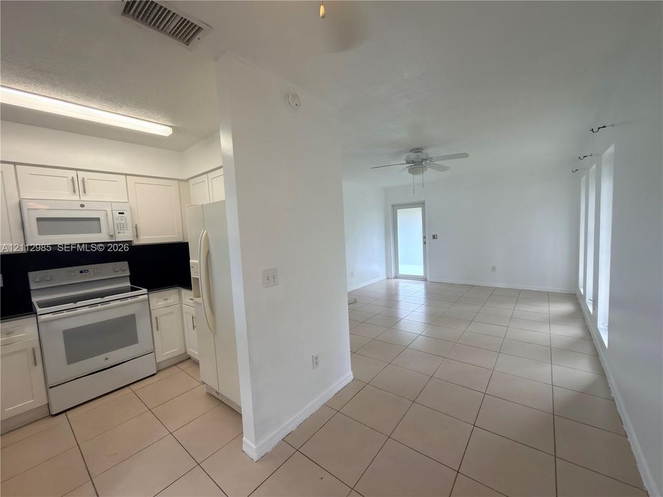 Kitchen featuring white cabinetry, high-contrast dark backsplash, and matching white appliances, complemented by tile flooring throughout the area and a ceiling fan