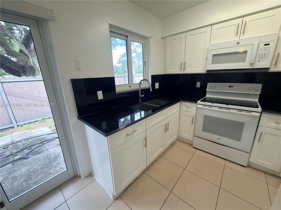 Kitchen featuring white cabinetry, dark stone-finish countertops, black backsplash, white appliance suite, and ceramic tile flooring