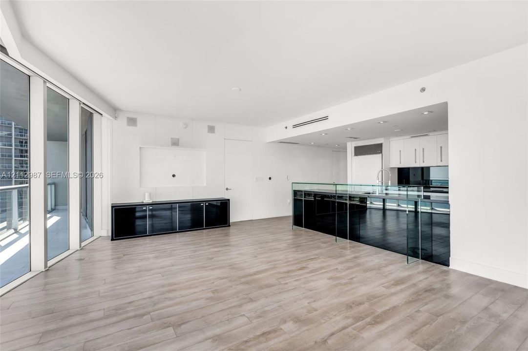 Open-concept floor plan featuring wood-finish flooring, floor-to-ceiling glass wall, built-in black lacquer cabinetry, and a kitchen island with a glass countertop
