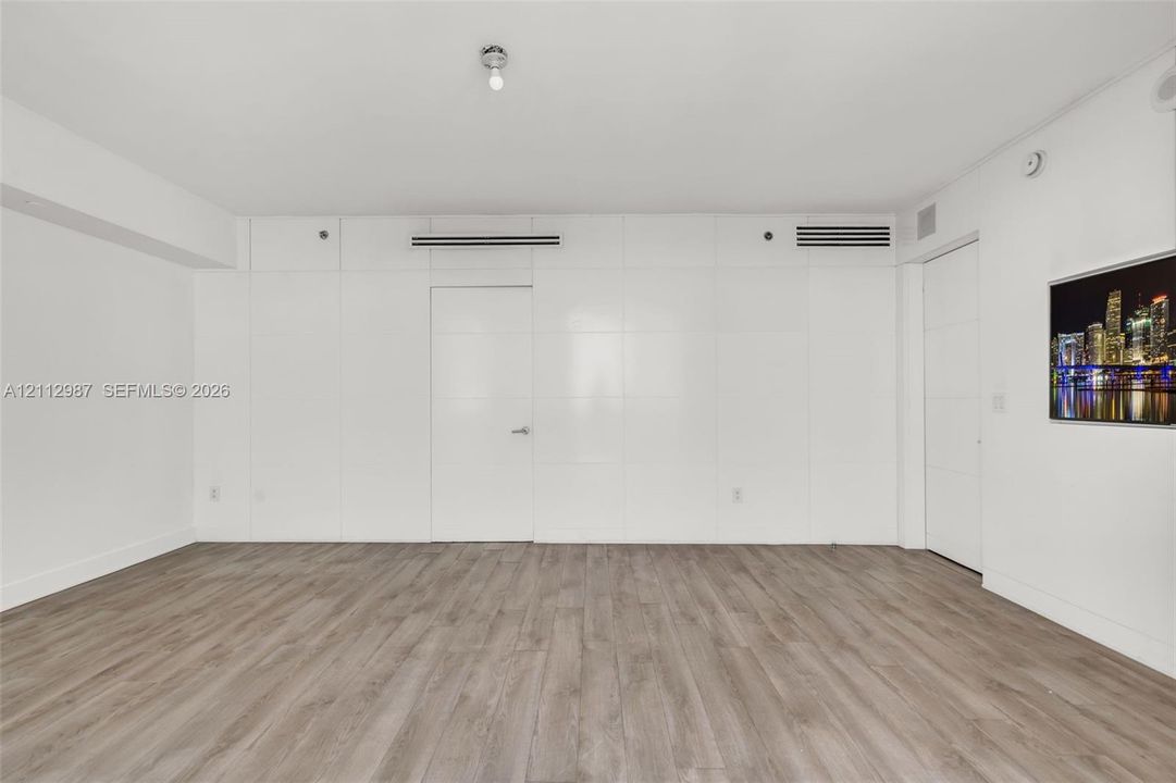 Modern living space featuring wood-finish flooring, full-height paneled wall detailing, and smooth-finish ceiling with integrated lighting