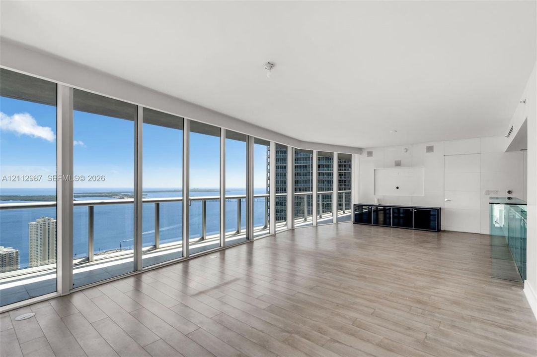 Floor-to-ceiling glass windows, wide-plank wood-finish flooring, and glass-railing balcony featuring expansive water and city skyline panoramas