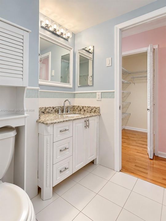 Bathroom featuring a white vanity with stone-surfaced countertop, integrated under-mount sink, tiled flooring, multi-light vanity fixture, and built-in cabinetry