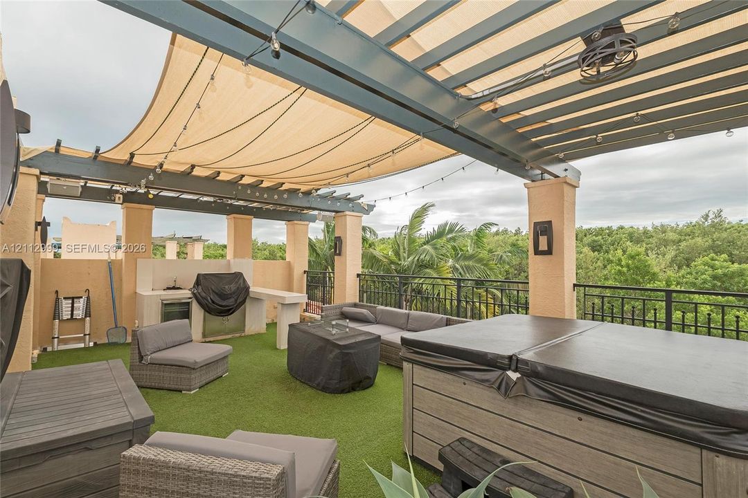Rooftop terrace featuring a covered pergola with a retractable shade canopy, built-in outdoor kitchen, integrated lighting, and a composite-finish hot tub