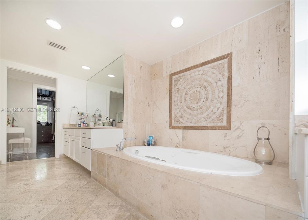 Soaking tub with a deck surround featuring stone tile cladding, wall-mounted mosaic tile inlay, recessed lighting, and stone flooring
