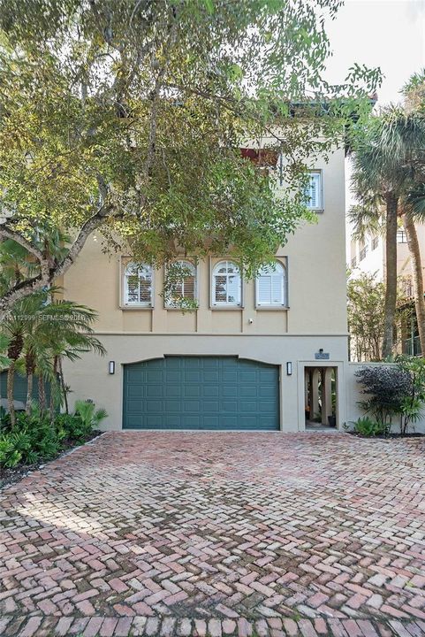 Stucco exterior featuring arched windows, a multi-level silhouette, a dedicated garage, and a brick-paved driveway