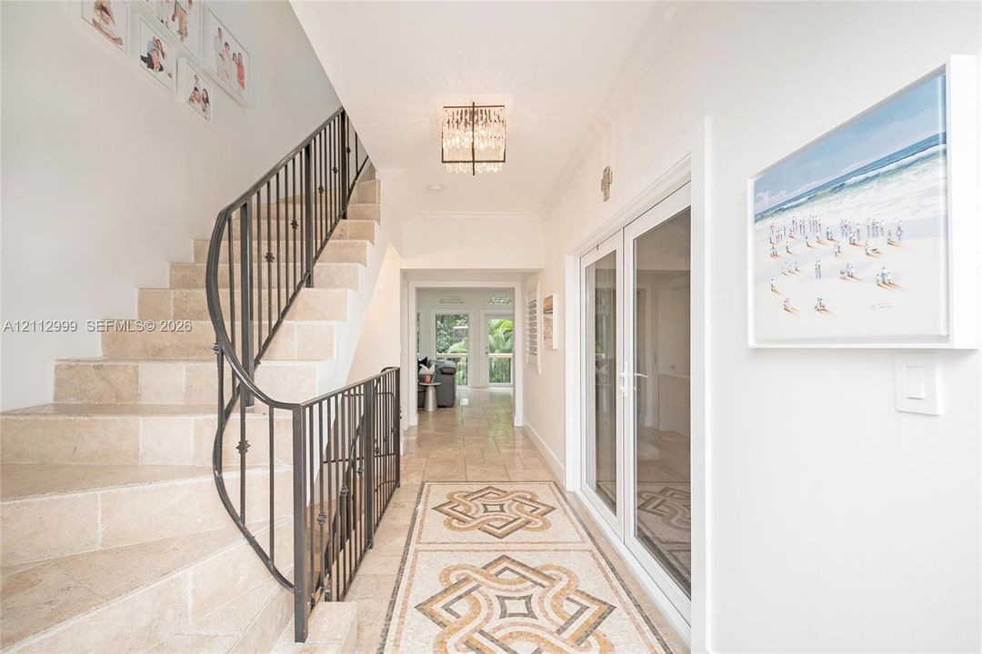 Foyer featuring stone stair treads, a decorative metal balustrade, intricate mosaic tile flooring inlay, and a flush-mount crystal chandelier