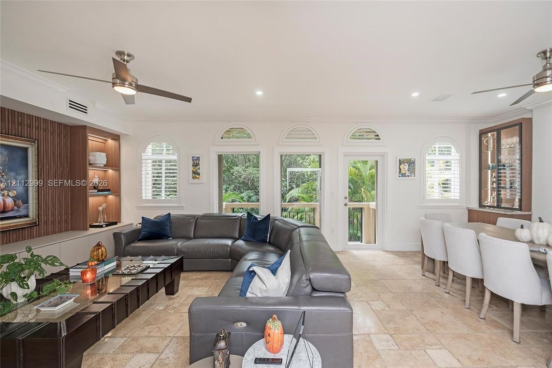 Open living space featuring stone flooring, arched windows, recessed lighting, built-in wooden display shelving, and dual ceiling fans