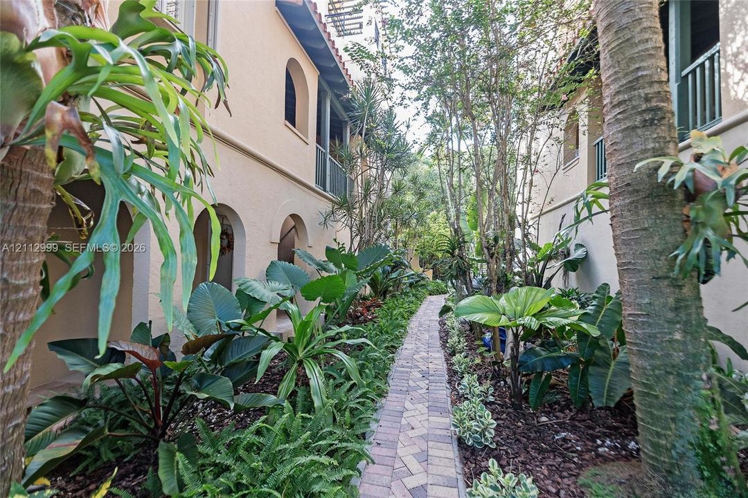 Stucco exterior featuring arched breezeways and second-story balcony railings, accented by a herringbone-patterned paver walkway and mature landscaping