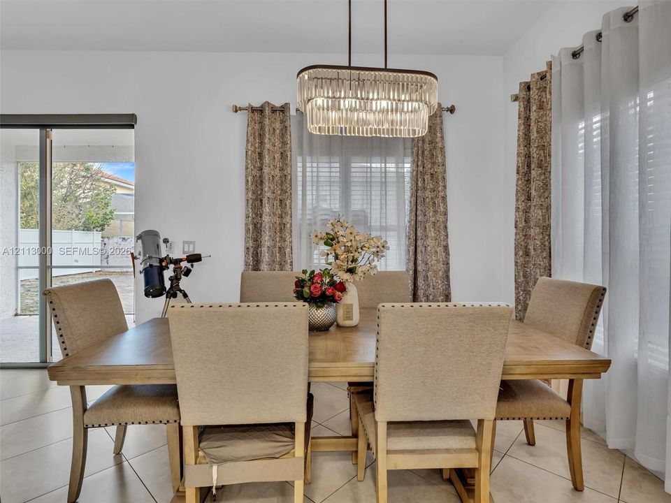 Dining area featuring large-format tile flooring, a tiered crystal chandelier, and sliding glass doors providing outdoor access