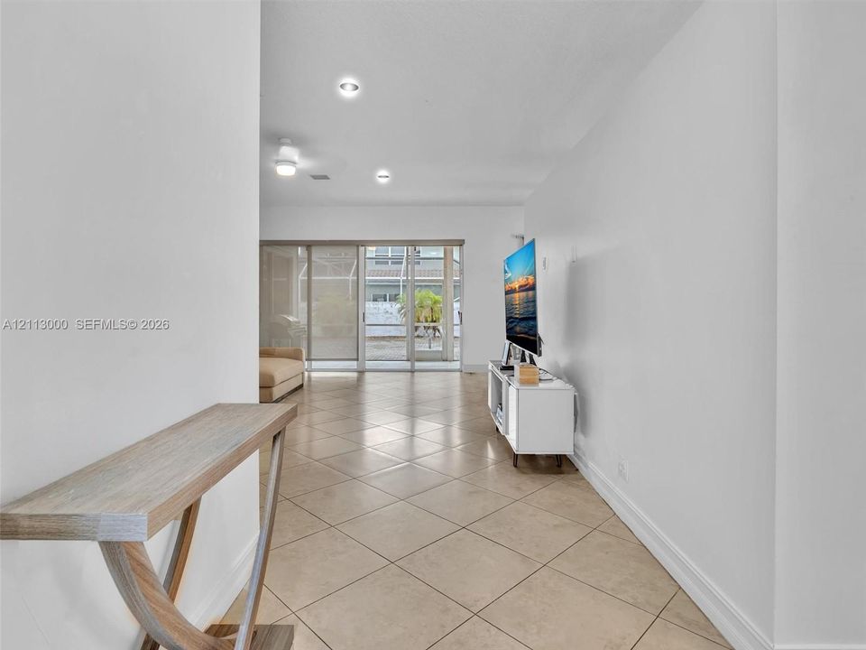 Neutral ceramic tile flooring, recessed ceiling lighting, and sliding glass doors leading to a screened-in enclosure