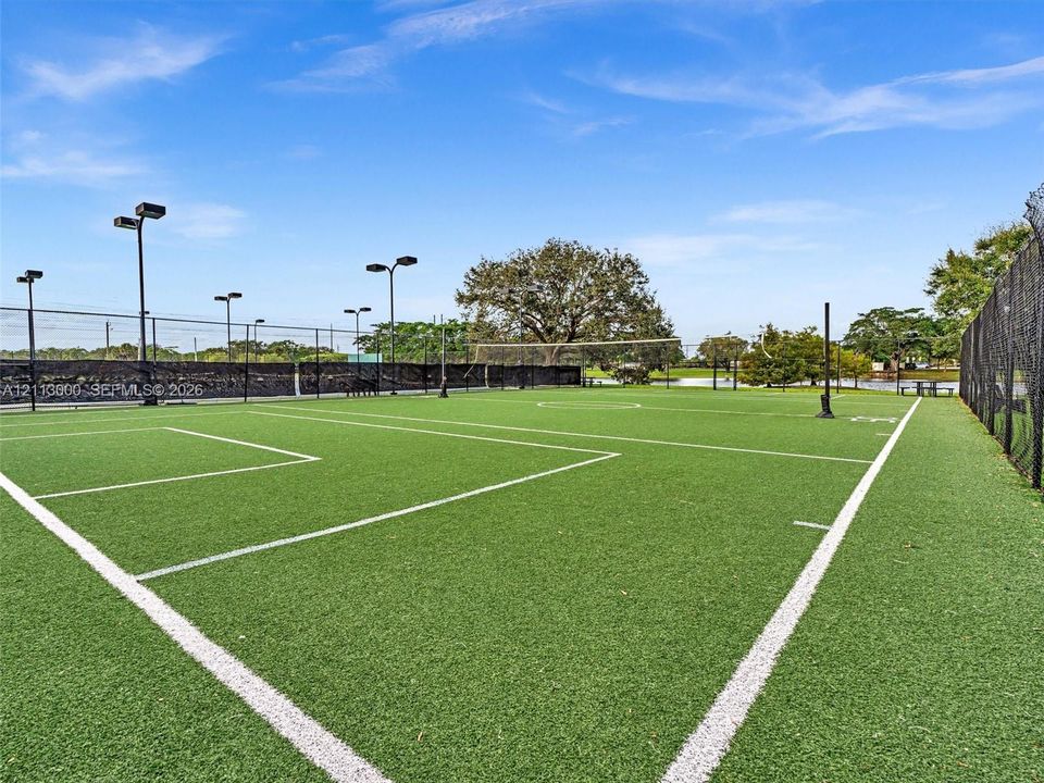 Synthetic turf court featuring permanent boundary markings, perimeter chain-link fencing, and elevated pole-mounted lighting