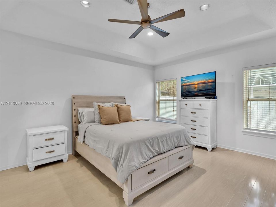 Tray ceiling with recessed lighting, multi-blade ceiling fan, and light-toned wood-finish flooring
