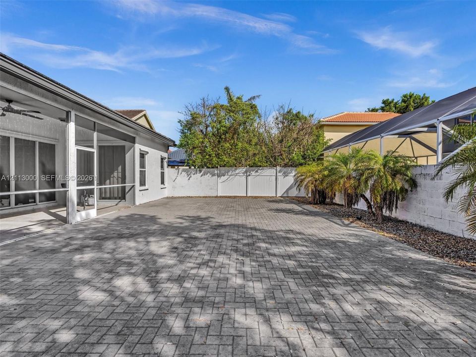 Screened-in covered lanai featuring paved patio flooring and a white privacy fence