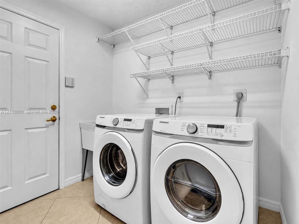 Laundry area featuring multi-tier wire shelving, integrated utility sink, and tile flooring