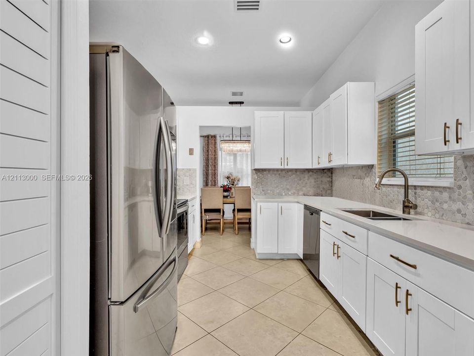Kitchen featuring white shaker-style cabinetry, stainless steel refrigerator, stone-composite countertops, mosaic tile backsplash, and tile flooring