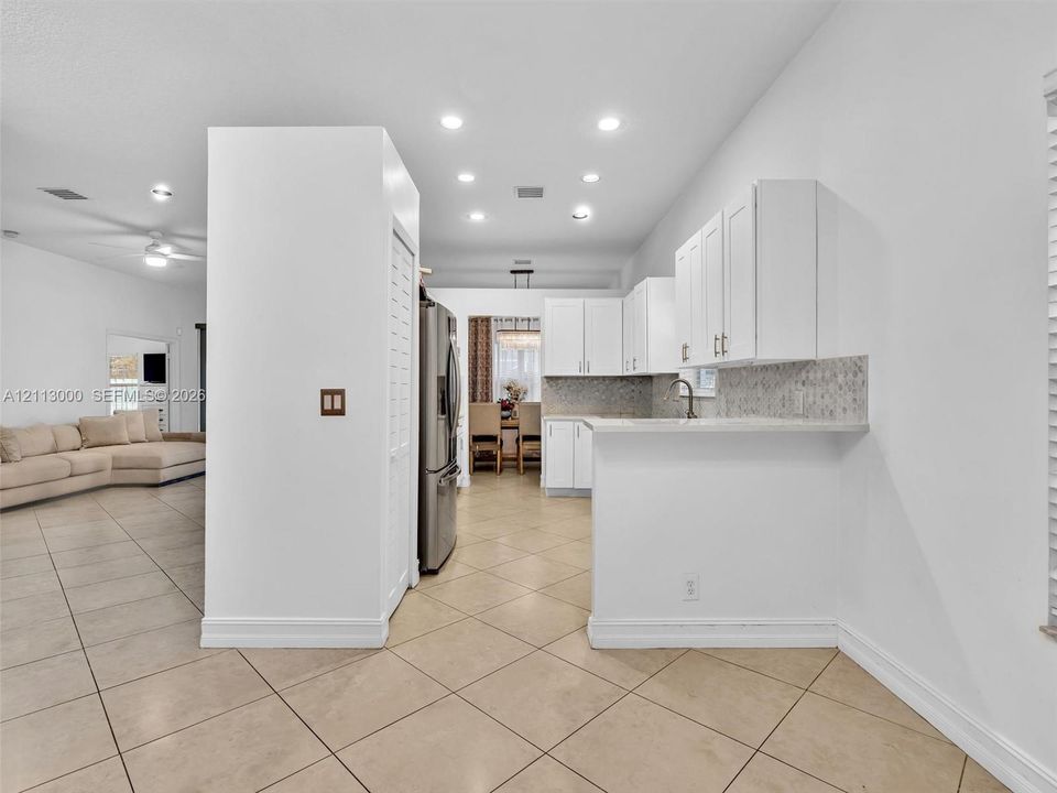 Kitchen featuring white cabinetry, solid-surface countertops, tile backsplash, stainless steel refrigerator, and recessed lighting