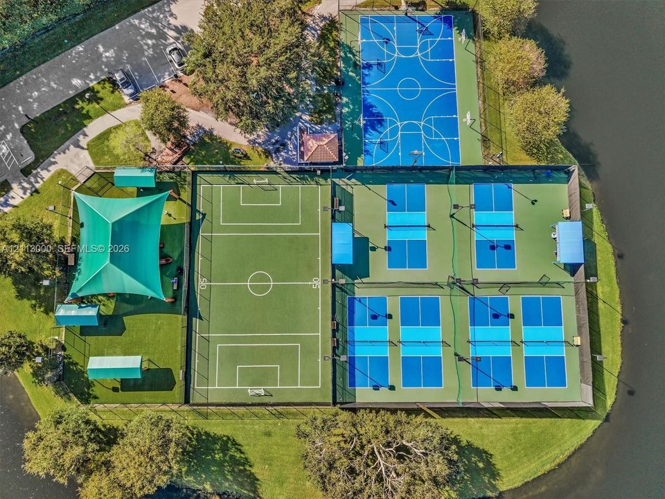 Recreational complex featuring a full-size basketball court, multi-purpose athletic field with sun shade canopy, and multiple pickleball courts situated along the waterfront
