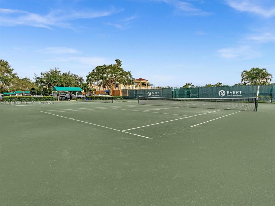 Hard-court tennis facility featuring perimeter privacy screening, professional-grade court surfacing, and integrated netting