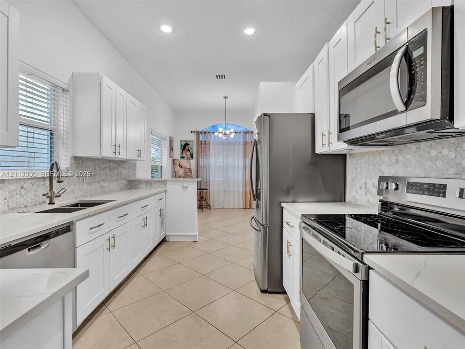 Kitchen featuring white shaker-style cabinetry, stainless steel appliances, quartz countertops, hexagonal mosaic tile backsplash, and tile flooring