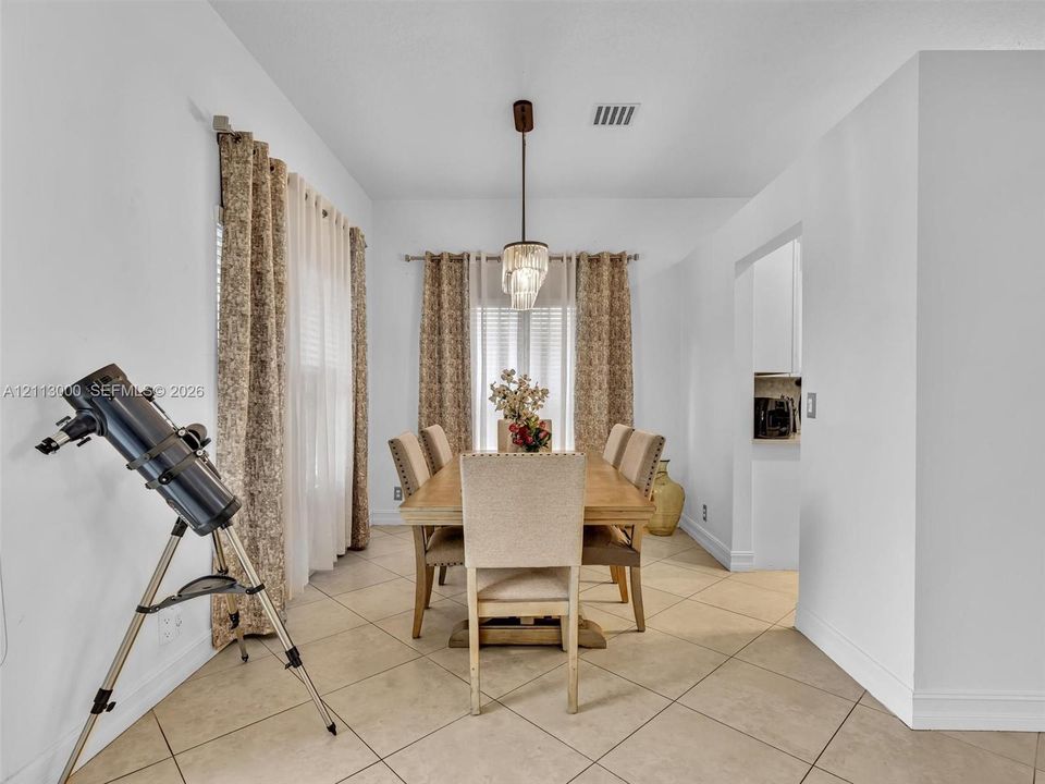 Dining area featuring large-format diagonal tile flooring, custom window drapery hardware, and a crystal-accented hanging light fixture
