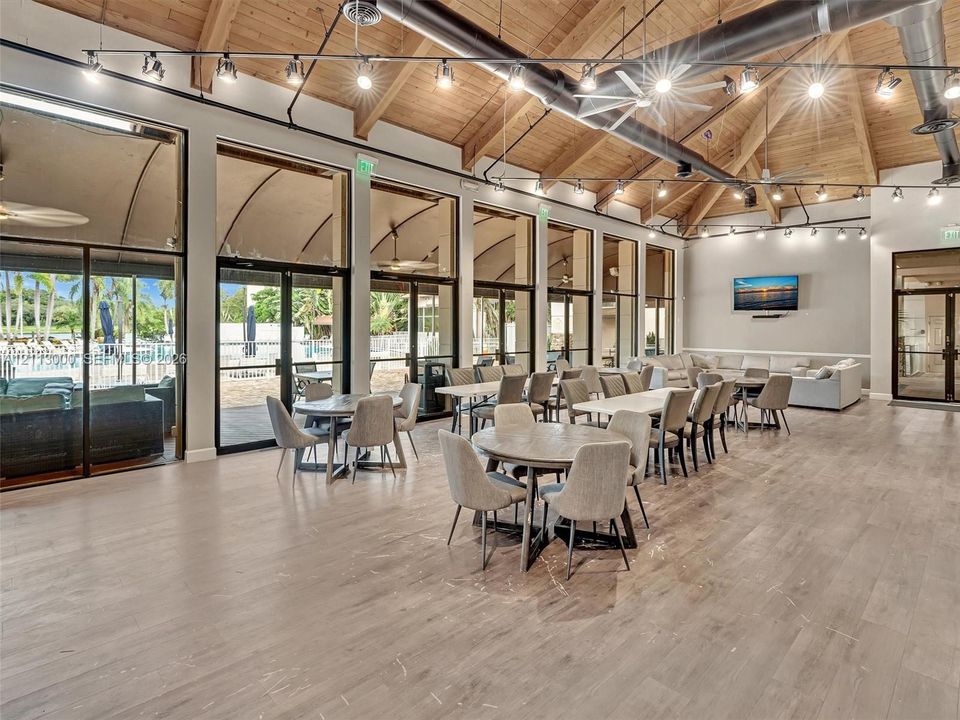 Exposed wood-beam vaulted ceiling, expansive floor-to-ceiling glass wall panels, industrial-style track lighting, and wood-finish flooring